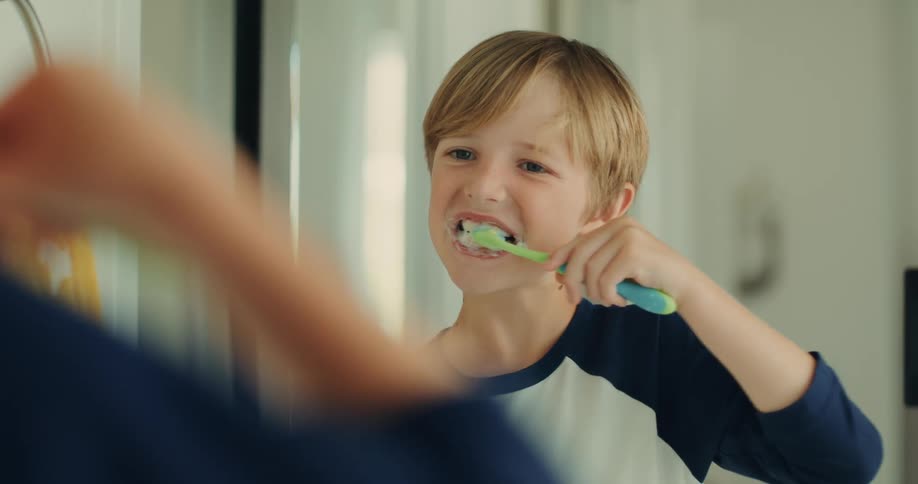 Blond boy brushing his teeth in front of the mirror in the bathroom