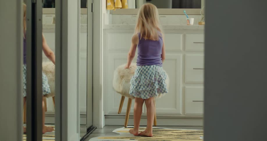 A little blonde girl jumping into a room grabs a stool and climbs up to see herself in the mirror