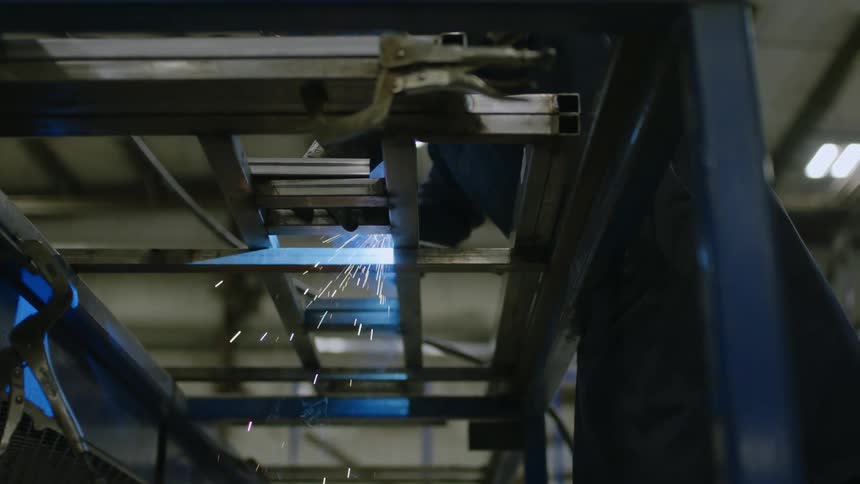 A person is welding a metal ladder and giving off several blue sparks