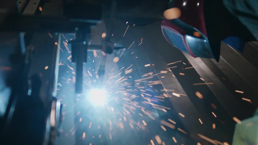 A person wearing a protective helmet welding on a metal plate and several sparks are coming out