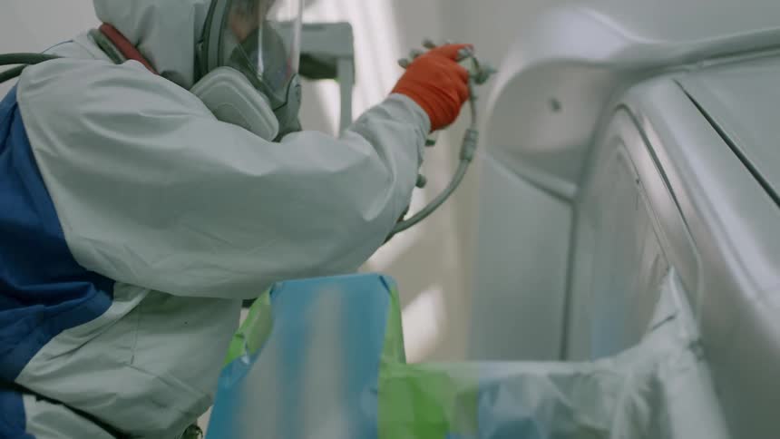 An employee expertly spray paints a vehicle inside of a garage