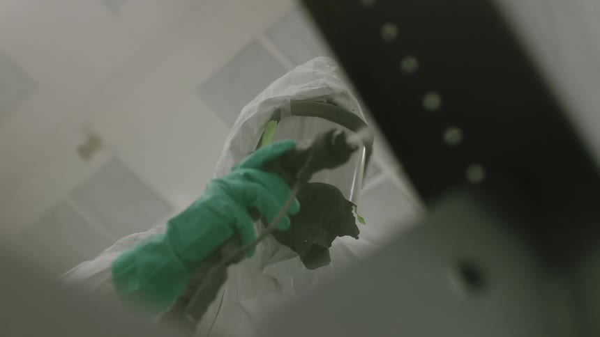A worker covered in protective clothing sprays paint out of a paint gun