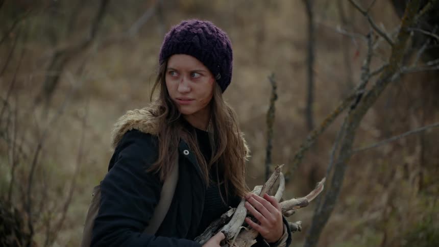 A young woman wearing a purple cap is worried looking to the side while holding a pile of dry twigs