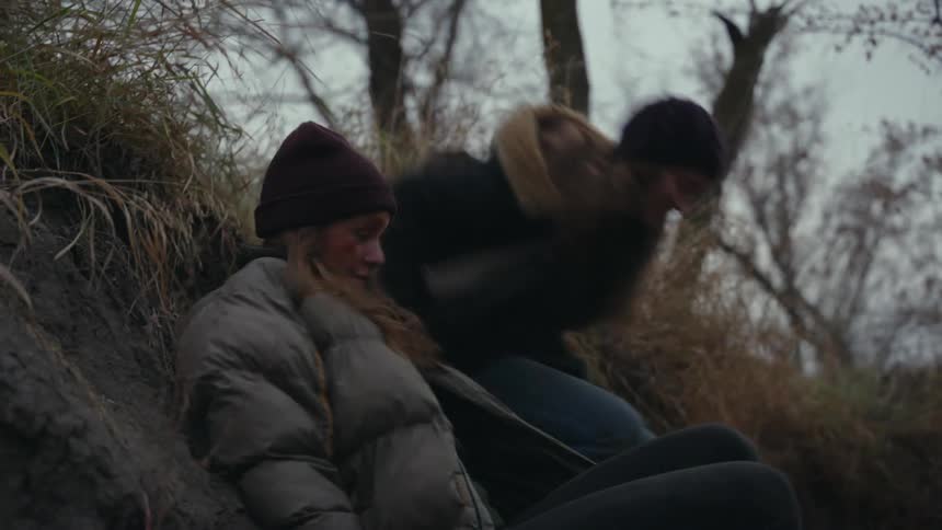 Two girls run through a barren forest in winter and hide in a ditch
