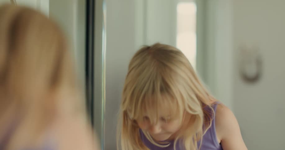 A young blonde girl brushes her teeth and spits