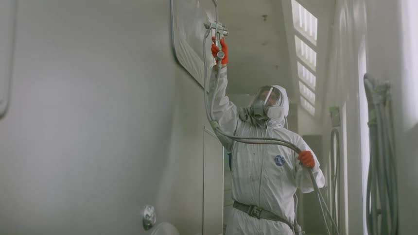 Person in protective suit painting the side of a vehicle with a hose