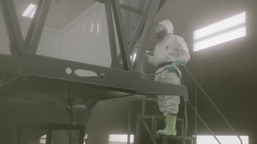Person wearing white protective clothing and mask performing painting in an upper indoor environment