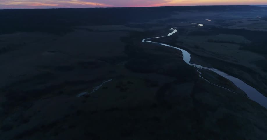 River winds through hilly terrain under a red tinted sky