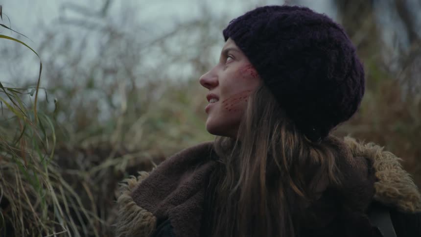 A woman with bruises on her face is sitting and then she gets up and climbs into a tall bush