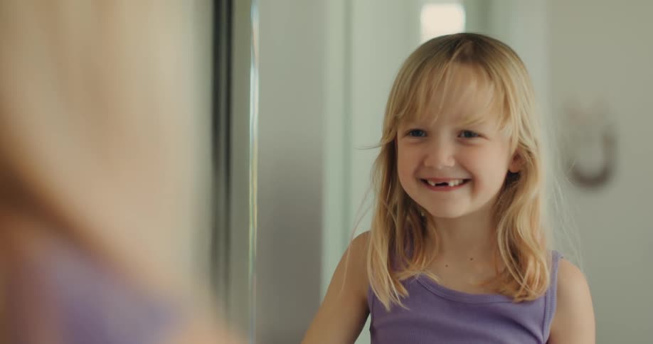 Little girl wiping her mouth on towel while smiling in front of mirror in bathroom