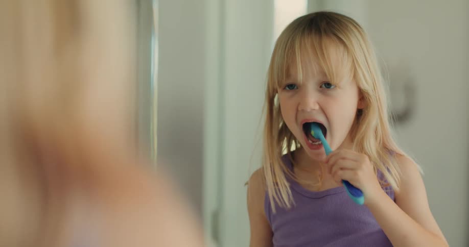 Portrait of a girl putting toothpaste on her brush and brushing her teeth in front of the mirror