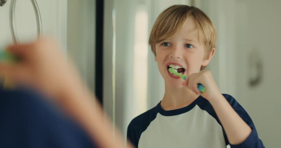Portrait of a little boy brushing his teeth in front of the mirror
