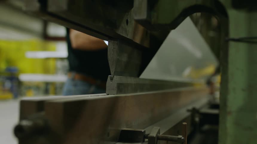 Factory worker uses machine to shape metal sheet