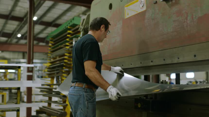 Man places a piece of sheet metal in the middle of a machine that opens in the center