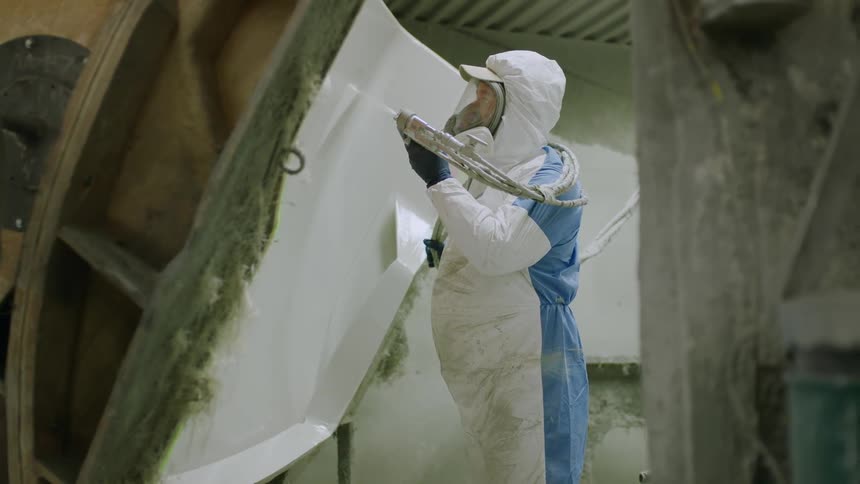 Person dressed in a white protective suit including a mask and gloves handling a painting tool