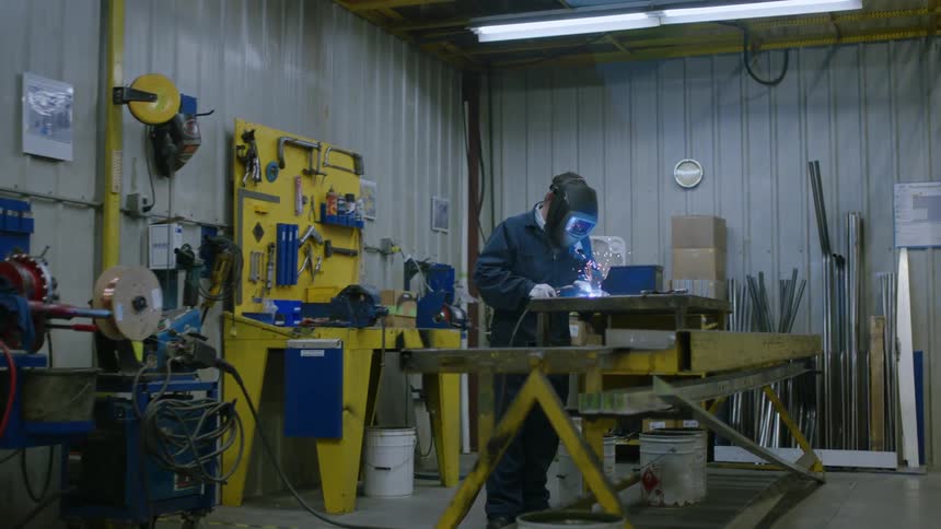 Person using welding equipment in a workshop surrounded by metal tools and materials