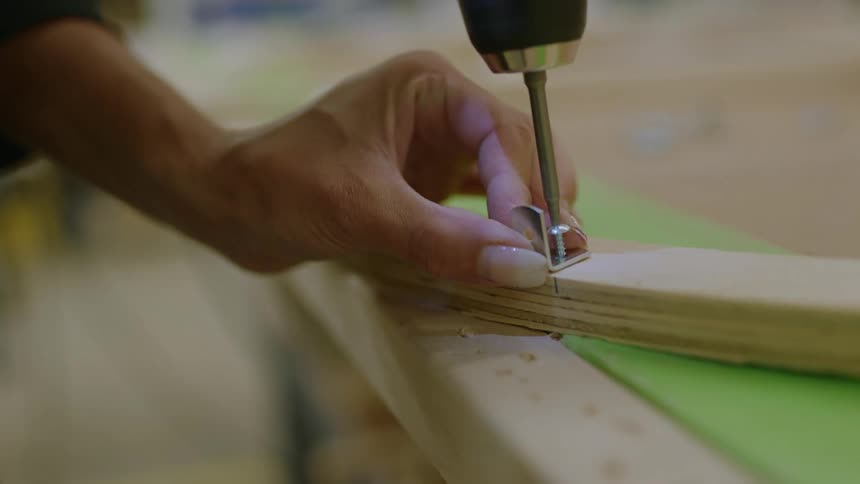 Woman uses a drill to attach a board with a screw