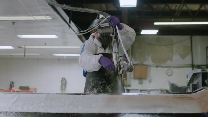 Man in protective clothing and mask using a tool and painting a plate