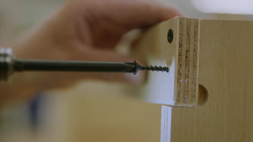 A person drills a screw into a piece of wood