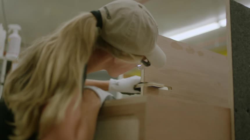 Female woodworker sands furniture under construction in a workshop