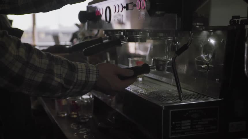 A barista is running water over a portafilter as he stands at an espresso machine