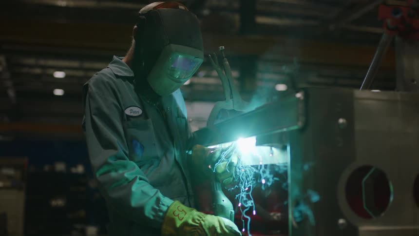 Mechanic stands in workshop and welds a machine part