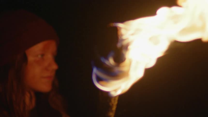 A girl holds a burning torch outside at night