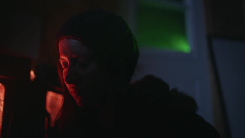 A young woman inside a dark place with a flare of green light passing behind her and she is distressed