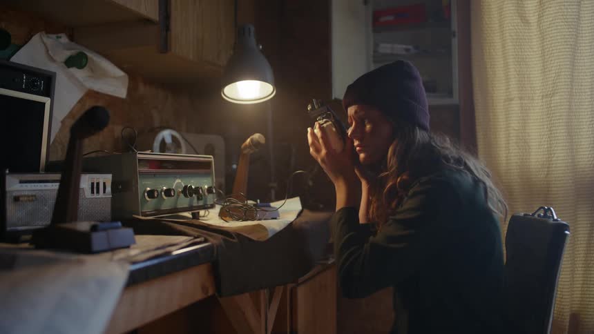 Two women wearing beanies are looking at an old radio and changing the buttons and one of them takes out a headphone to listen