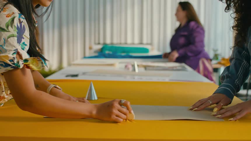 A fashion designer traces pattern over a piece of yellow fabric in her studio