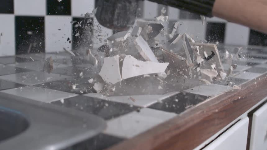 A sledge hammer is crashing down on a countertop in a kitchen