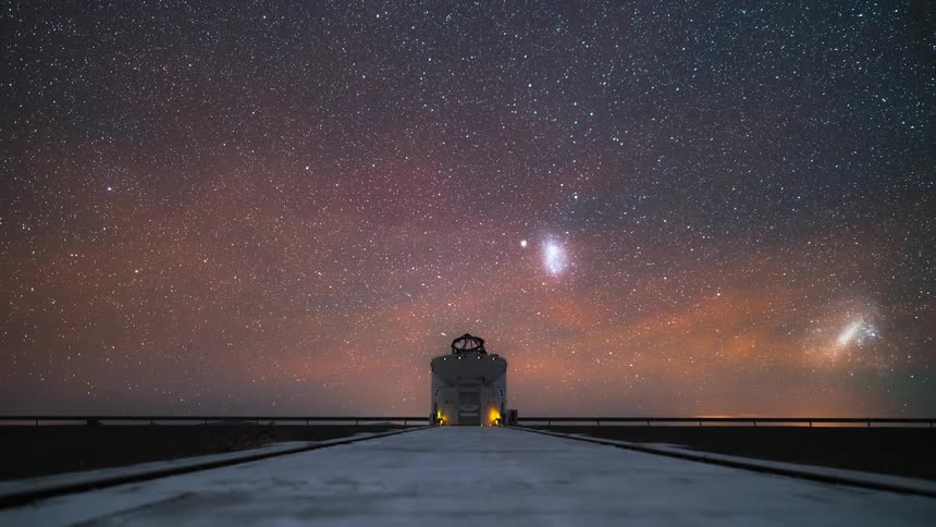 Observatory under a starry night sky with the milky way visible and an orange light on the horizon