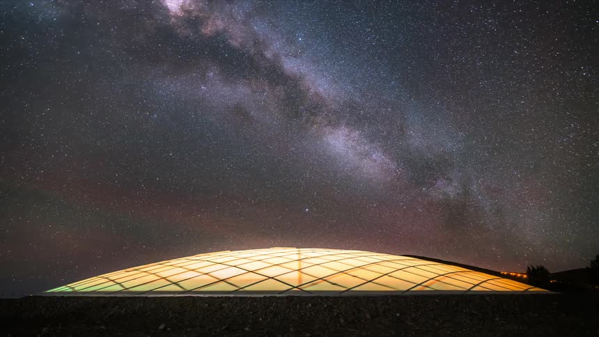 The milky way galaxy moves through the sky over a large lighted dome