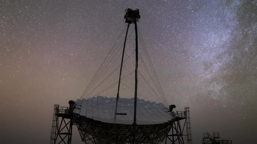 A large radio telescope silhouetted against a starry night sky scanning the cosmos