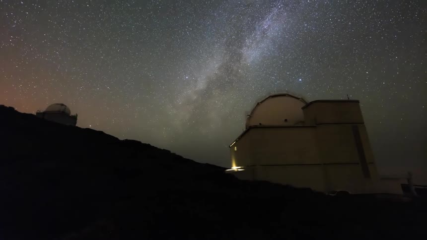 A round observatory pointed at the sky is turning and the sky is full of stars