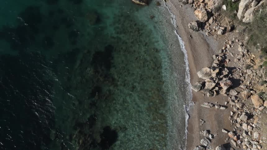 Overhead aerial shot of a rocky beach with clear blue water
