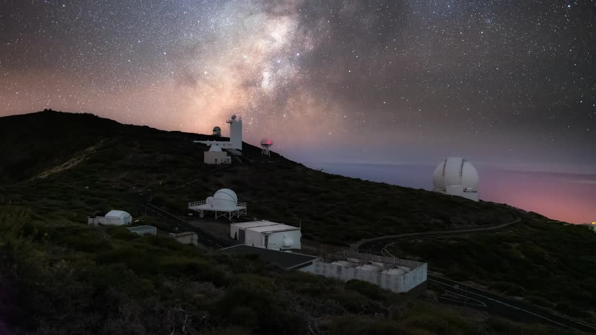 Several buildings making up an observatory on a mountainside underneath the milky way galaxy in the night sky
