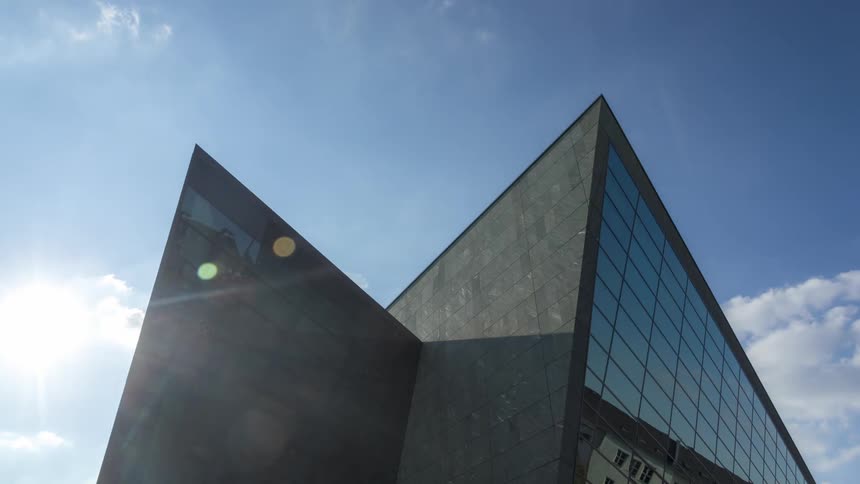 Building in a metropolis mirrored against a blue sky with clouds passing by