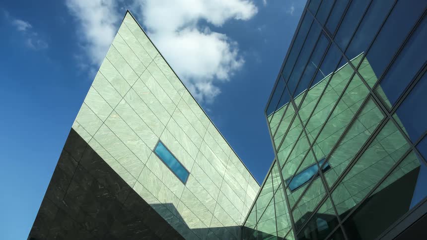 Modern architectural structure with glass surfaces and reflective metal panels under a blue sky with scattered clouds