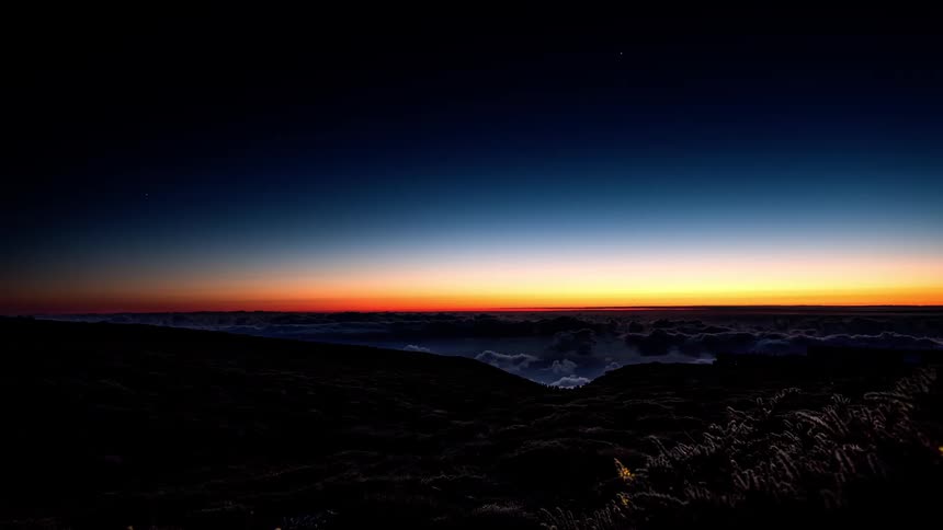 Orange sun setting on the horizon with a day darkening in a sea of clouds passing close to the mountains