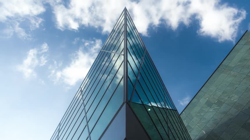 Reflective facade of sharp edged building reflects the passing clouds
