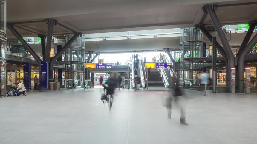 A timelapse of several people passing through a terminal with a white floor and several glass structures and a staircase