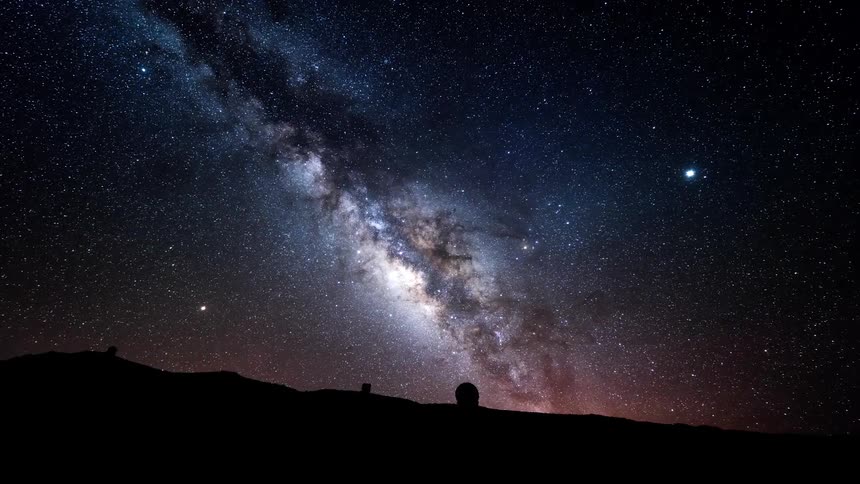An observatory sitting on a sloping high area as outer space passes by overhead