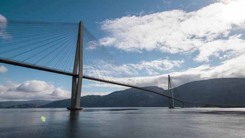 White clouds move over a suspension bridge set over water