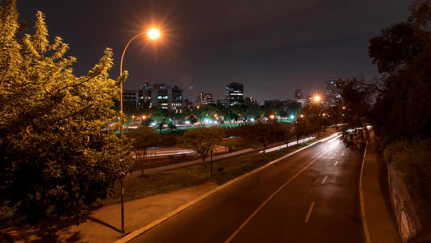 An asphalt street with several cars passing by at night when you can only see the lights of the headlights