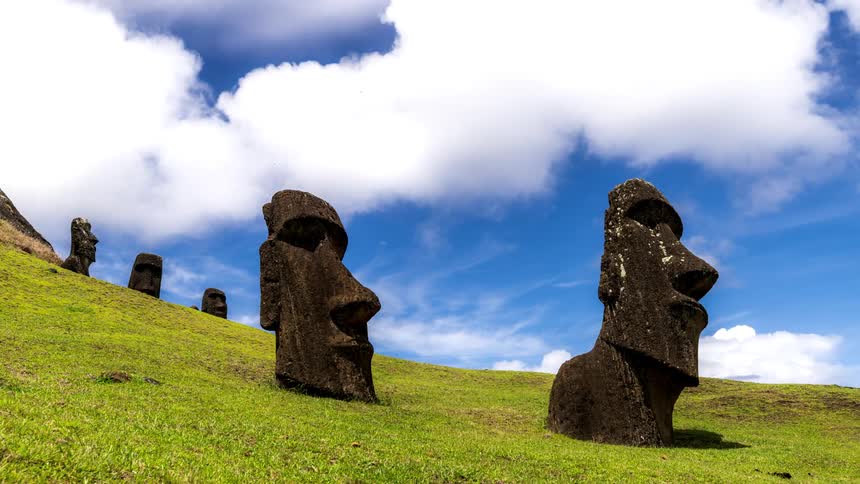 Two heads of moai statues on easter island in a green field and the sky is passing white clouds