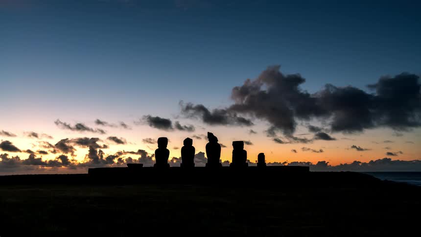 Moai statues silhouetted against a colorful sky at dusk
