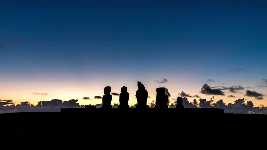 A silhouette of five statues against the sky with several clouds passing by
