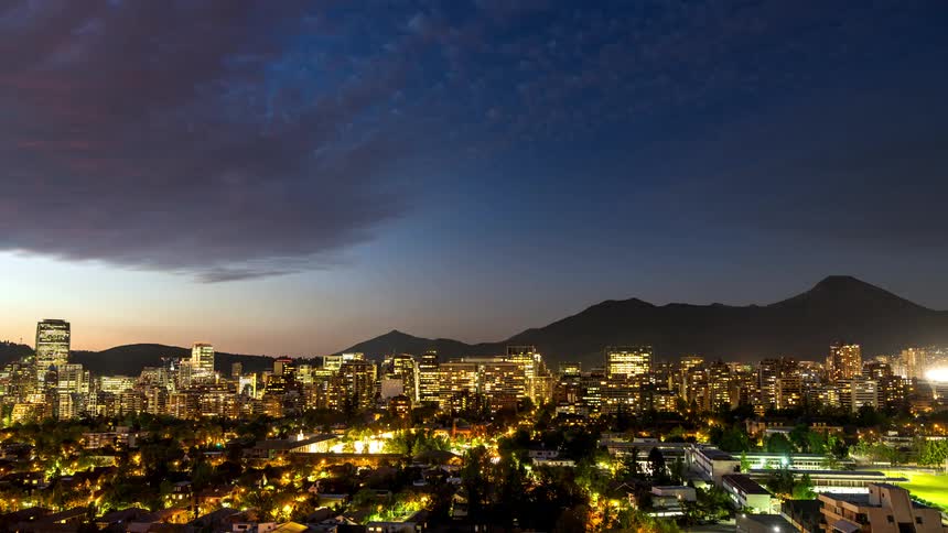 A city with a mountain range in the background at sunset clouds move overhead before the sun sets