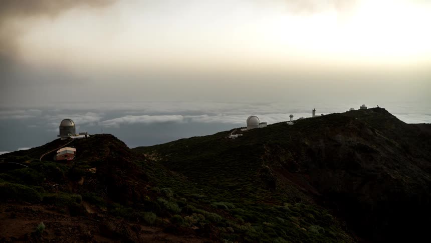 Observatories on top of a mountain during a beautiful sunset with clouds below the level of the mountain